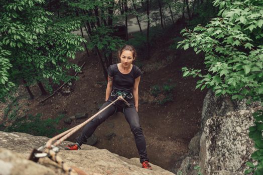 Climber young woman wearing in safety equipment standing on stone rock in summer outdoor, top view