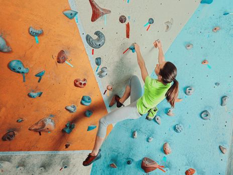 Beautiful sporty young woman climbing on practical wall in gym, bouldering
