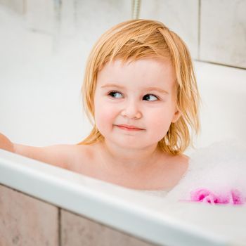 cute two year old baby bathes in a bath with foam closeup