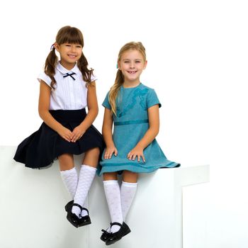 Full length shot of cute sitting girls. Above view of adorable sisters posing against white background. One of girls in stylish blue dress, the other in school uniform. Elementary school students