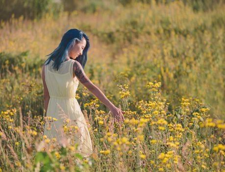 Beautiful young woman with blue hair walking on flower field in summer