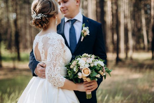 the bride and groom are walking in a pine forest on a bright day