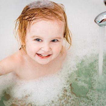 cute two year old baby bathes in a bath with foam closeup