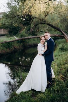 the groom and the bride are walking in the forest near a narrow river on a bright day