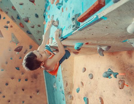 Free climber boy climbing on artificial boulders in gym