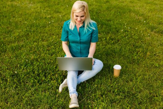 beautiful young blond woman with a laptop in the park on a warm summer day