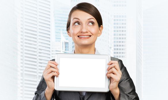 Businesswoman holding tablet computer with blank screen. Smiling woman in business suit show tablet PC and looking upward. Corporate businessperson on downtown background. Digital technology layout