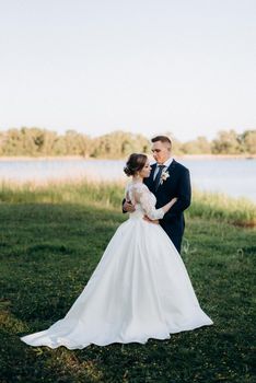 the groom and the bride are walking in the forest near a narrow river on a bright day