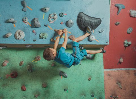 Climber boy exercises on artificial boulders wall in gym