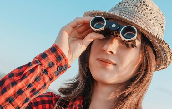 Smiling traveler young woman looking through binoculars outdoor