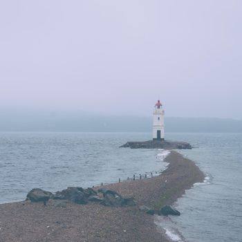 Lonely lighthouse on foreland in the sea. Image with blue toning color