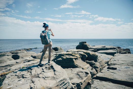 Traveler girl taking photographs beautiful seascape with smartphone on rocky coast in summer