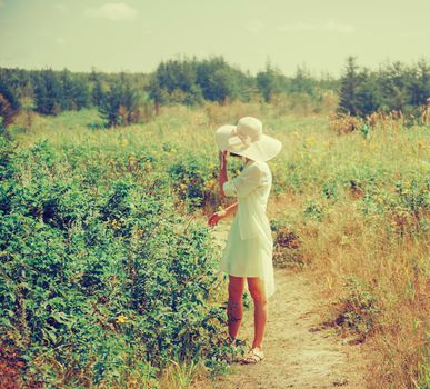 Beautiful woman in a hat with wide brim and dress walking outdoor in summer. Image with instagram color effect