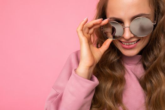 Closeup photo of pretty positive smiling young blonde curly woman isolated over pink background wall wearing casual pink sport clothes and stylish sunglasses looking at camera. copy space