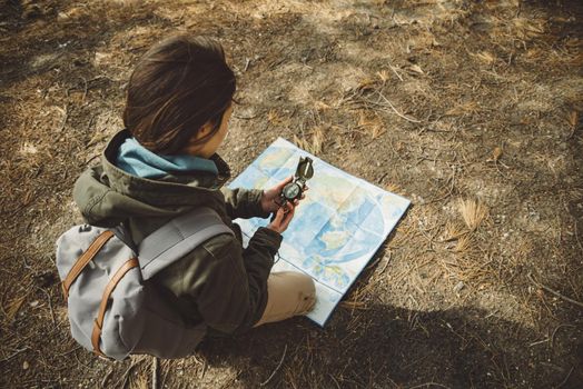 Traveler young woman with backpack searching direction with a compass on background of map in the forest. Focus on compass