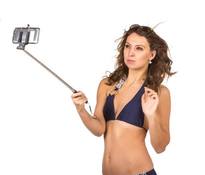 Close up portrait of Tanned adult woman in blue bikini swimsuit taking herself photo with big smatphone on stick