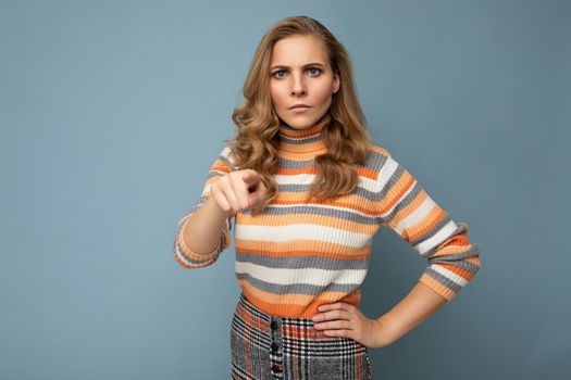 Portrait of angry dissatisfied young beautiful blonde curly woman with sincere emotions wearing stylish striped sweater isolated on blue background with empty space and abusing.