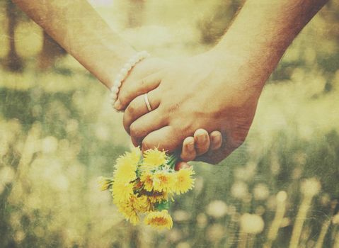 Young loving couple holding hands each other with bouquet of yellow dandelions in summer park, view of hands. Vintage image