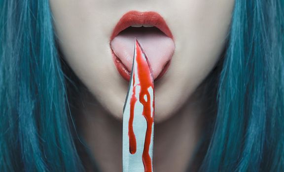 Dangerous young woman licking a knife in blood. Halloween or horror theme