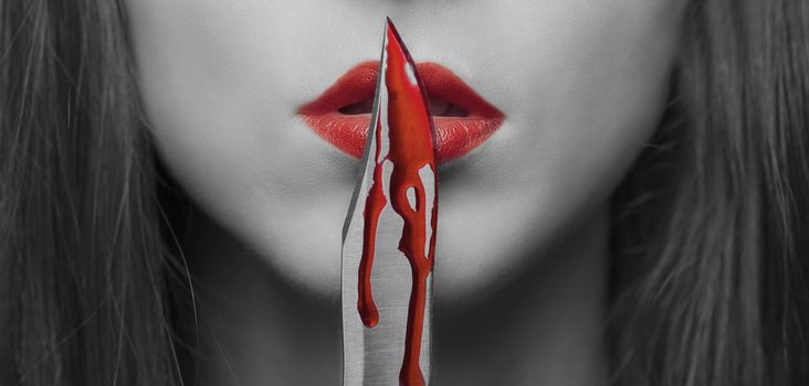 Dangerous young woman kissing a knife in blood. Halloween or horror theme. Black and white image with red elements