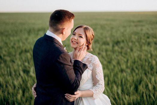 the groom and the bride walk along the wheat green field on a bright day