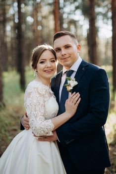 the bride and groom are walking in a pine forest on a bright day