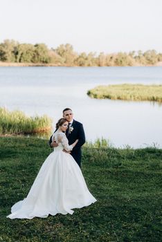 the groom and the bride are walking in the forest near a narrow river on a bright day