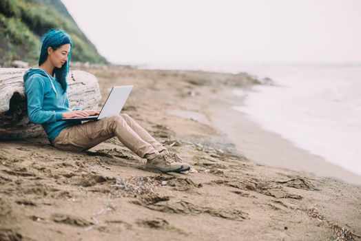 Freelancer young beautiful woman working on laptop on sand beach near the sea