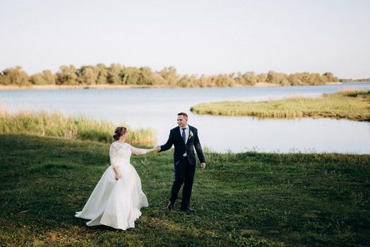 the groom and the bride are walking in the forest near a narrow river on a bright day