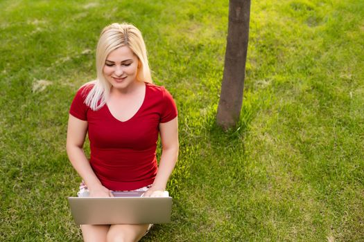 cheerful young woman browsing internet on her laptop outdoors at the park