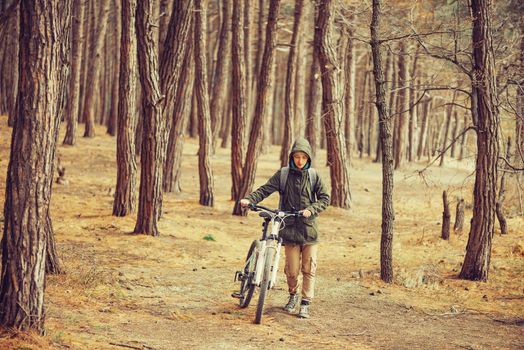 Hiker woman with backpack walking with a bicycle in pine forest, front view
