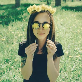 Smiling beautiful girl in wreath of yellow dandelions closed her eyes with dandelions in summer park, concept of summer mood