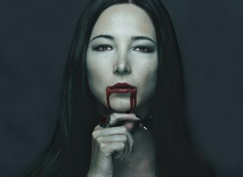 Dark portrait of beautiful young woman with vampire halloween make-up. Halloween or horror theme