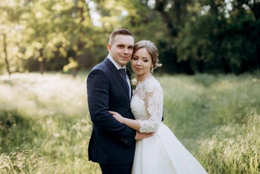 the groom and the bride are walking in the forest near a narrow river on a bright day