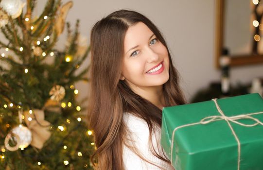 Christmas holiday and sustainable gifts concept. Happy smiling woman holding wrapped present with eco-friendly green wrapping paper.