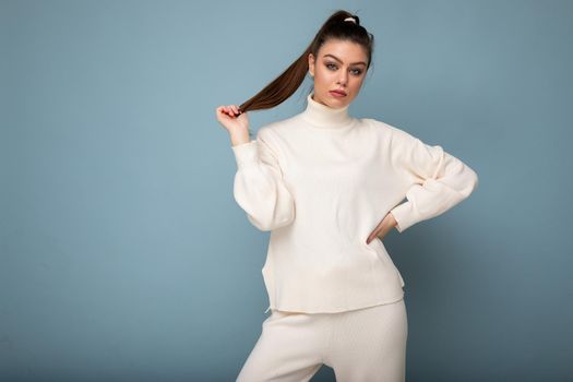Young beautiful european fashion woman wearing white sweater isolated over blue background with serious expression on face. Empty space