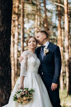 the bride and groom are walking in a pine forest on a bright day