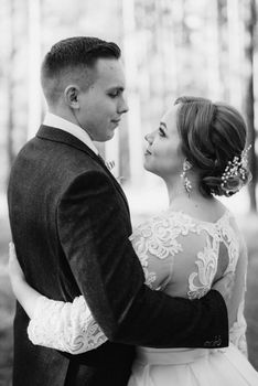 the bride and groom are walking in a pine forest on a bright day