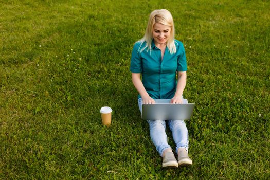 Top view of woman sitting in park on the green grass with laptop, hands on keyboard. Computer screen mockup. Student studying outdoors. Copy space for text