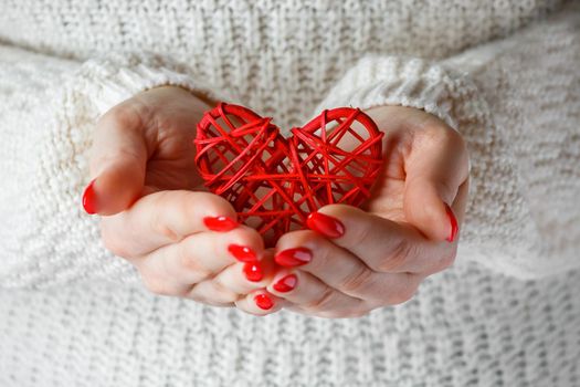 Heart in the hands of a woman. A young woman in a white sweater holds a red heart in her hands. A symbol of health care.