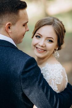 the bride and groom are walking in a pine forest on a bright day