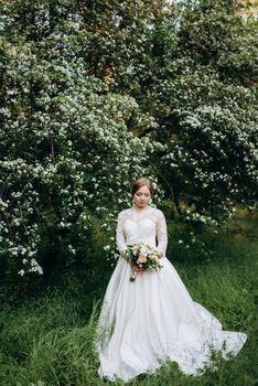 bride with a wedding bouquet in the forest near the bushes blooming with white flowers