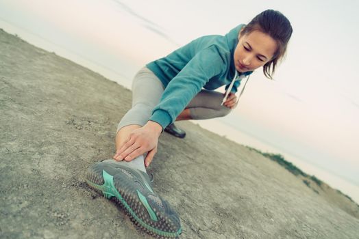 Girl stretching her legs and preparing to run on coast in summer. Concept of healthy lifestyle