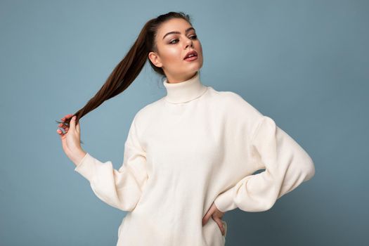 Young fascinating sexy caucasian fashion brunette woman wearing casual white sweater poising isolated on blue background wall.