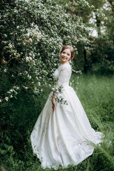 bride with a wedding bouquet in the forest near the bushes blooming with white flowers