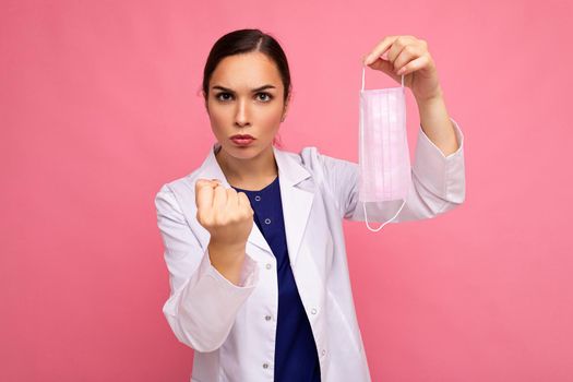 Caucasian woman showing protection face mask isolated on pink background and showing fist. Coronavirus or Covid-19 Concept.