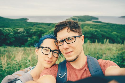 Traveler young loving couple doing selfie in mountains in summer. Girl with blue hair