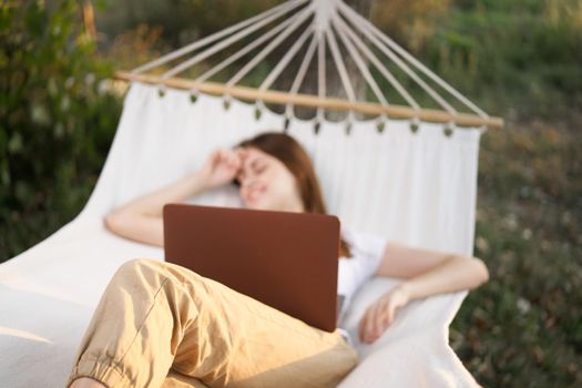 woman outdoors with laptop lies in hammock leisure technology. High quality photo