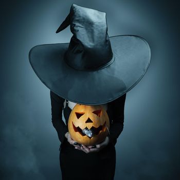 Halloween witch holding a pumpkin, which sits inside a rat