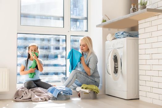 Happy housewife and her daughter with linen near washing machine